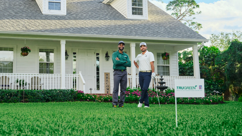 Jason Day with a TruGreen specialist smiling on a lawn with a TruGreen flag in the foreground.