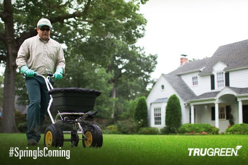 <p>TruGreen lawn specialist using a seed spreading machine on a lawn</p>