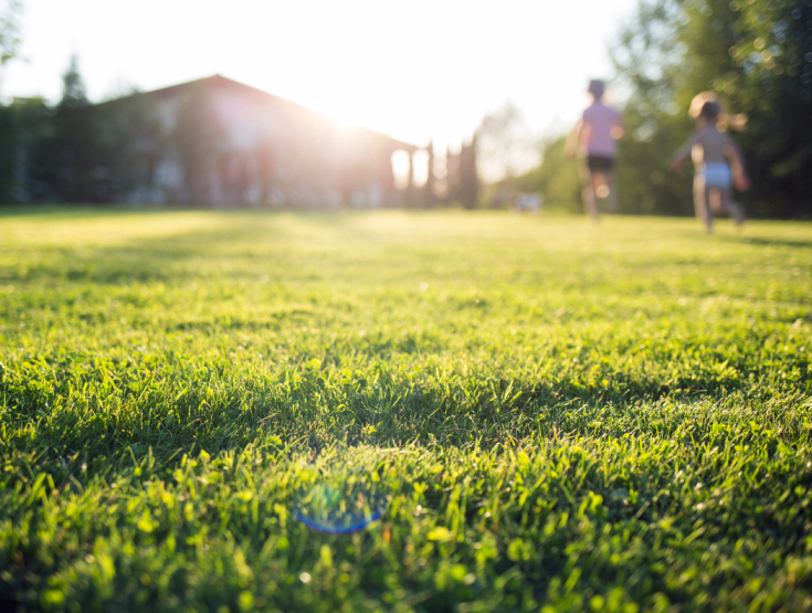 Children running on a real grass lawn in front of a house with the sun shining behind it