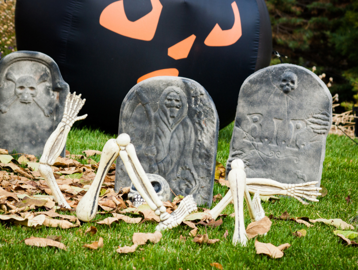 Faux gravestones with a faux skeleton and leaves on a lawn