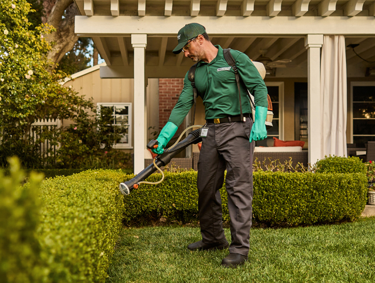 TruGreen specialist spraying pest control in front of a home