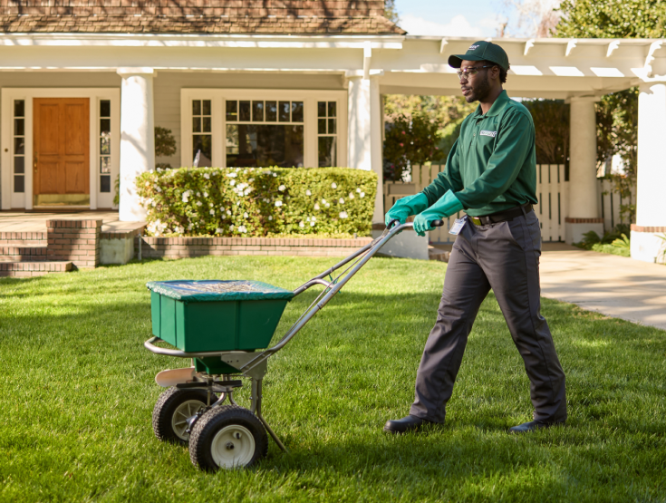 A TruGreen specialist using a spreader to put fertilizer on a lawn