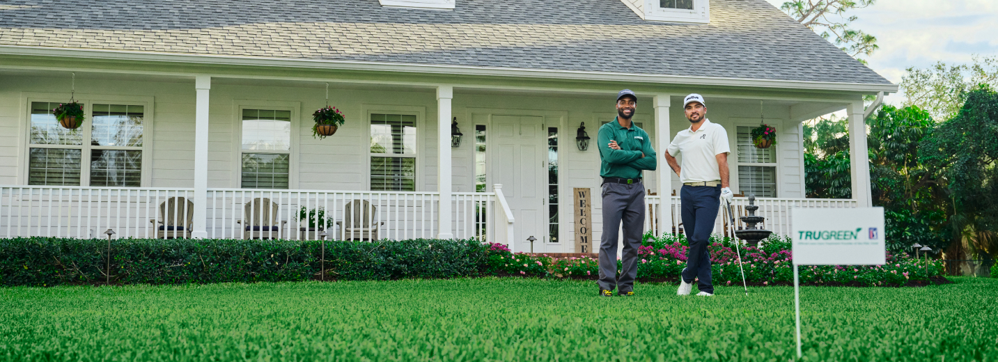 Jason Day with a TruGreen specialist smiling on a lawn with a TruGreen flag in the foreground.