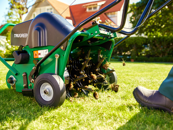 TruGreen specialist pushing an aerator over a lawn