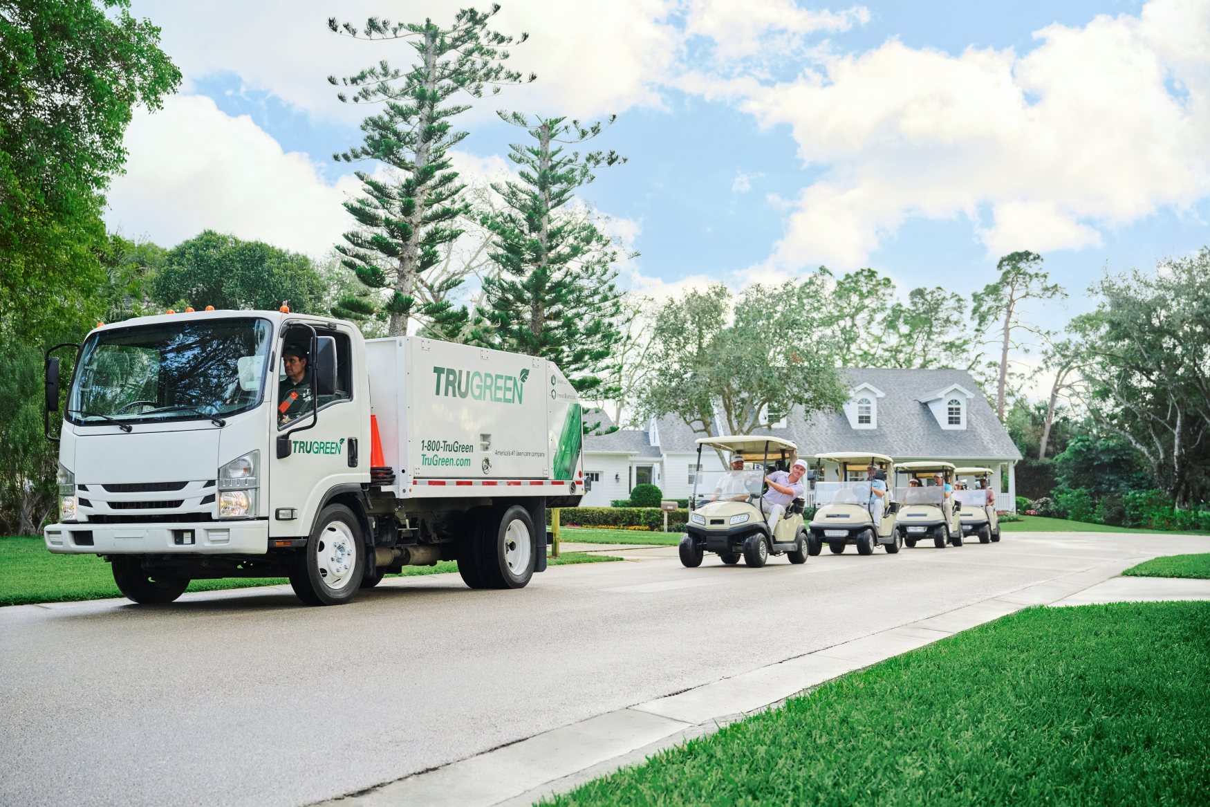 TruGreen truck driving and being followed by golf carts.